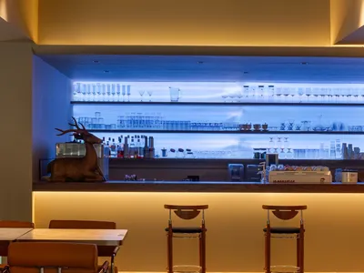 A stylish modern restaurant bar with wooden furniture, glass shelves, and concrete accents.