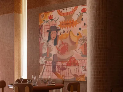 A café interior with a warm color palette, featuring chairs and tables arranged around a round table, and a colorful mural on
