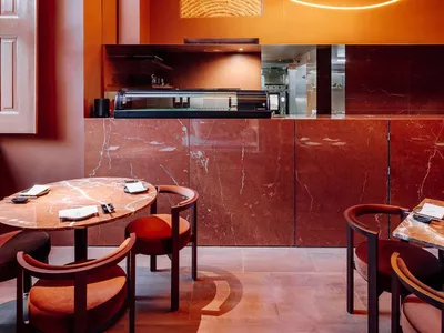 A modern restaurant interior featuring marble countertops, steel accents, and neon lighting fixtures.