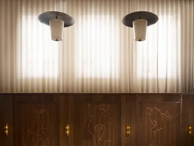 A modern bar and restaurant interior with wood-paneled walls, marble tables, and fabric-covered chairs.
