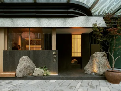 A modern restaurant exterior featuring large stones and a stone wall with a sign.