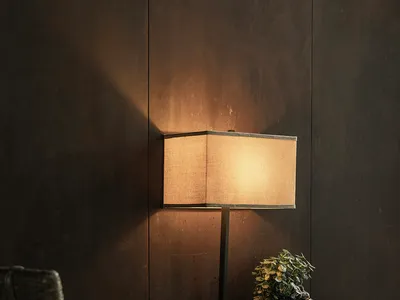 A modern desk lamp with a wooden base and a fabric lampshade illuminated in a home office setting.