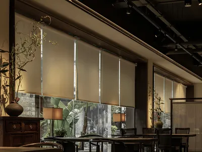 Interior of an industrial-themed restaurant with wooden tables and chairs, glass walls, and natural light.