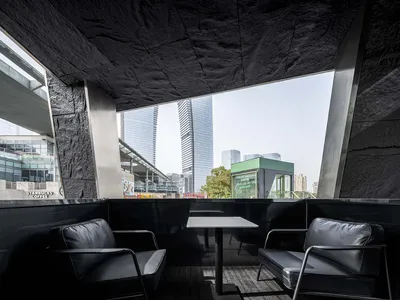 Modern industrial restaurant terrace made of concrete with metal seating and a large window overlooking urban buildings.