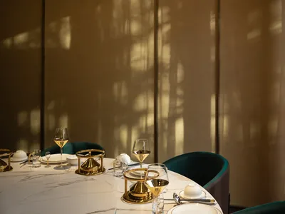 A minimalist restaurant dining room featuring white marble tables, gold accents, and elegant place settings.