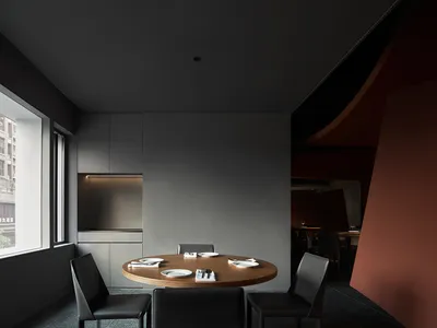 Modern minimalist restaurant dining room with a round wooden table, black leather chairs, and sleek metal accents.
