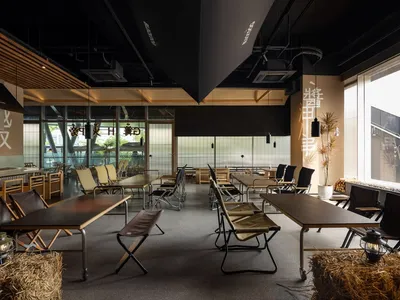 Contemporary restaurant interior featuring cement walls, wooden tables, and black metal chairs.
