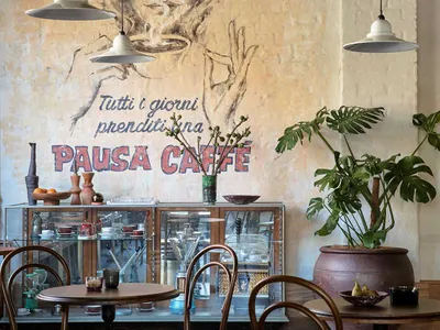 A cafe interior featuring wooden furniture, concrete walls, and potted plants.