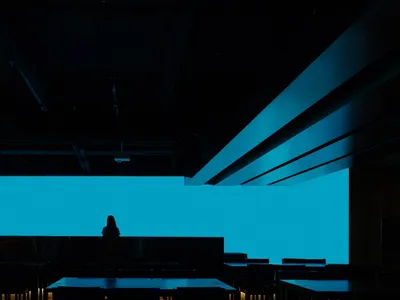 A modern restaurant interior with dark steel tables and seating, illuminated by a large blue screen.