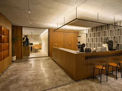 A coffee shop with a wooden counter and a concrete floor, featuring coffee-making equipment and seating.