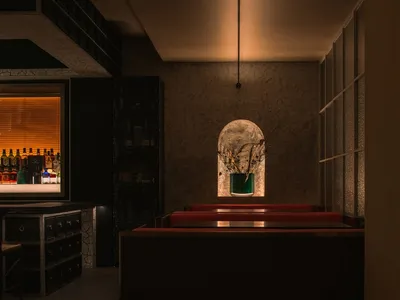 A dimly lit restaurant interior with industrial design elements, featuring a concrete floor and a bar counter in the backgrou