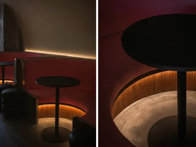 Round tables with red leather seating and concrete flooring in a modern restaurant bar setting with soft lighting.