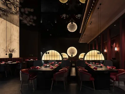 A modern restaurant interior with dark wooden tables and chairs, circular glass windows, and red leather seats.