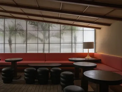 Modern restaurant interior with fabric seating, wood tables, metal stools, and plants.