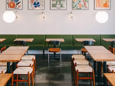 Interior design of a cafe featuring wooden tables, fabric chairs, and floral posters on the wall.