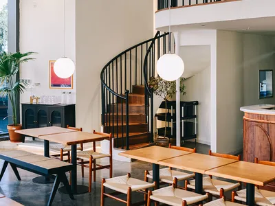 Industrial-style restaurant interior with wooden tables, metal chairs, and spiral staircase.