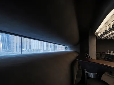 A modern restaurant bar counter with a sleek, curved concrete design featuring hanging lights.