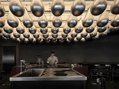A minimalist bar with metal and concrete finishes and a modern lighting installation featuring hanging glass elements.