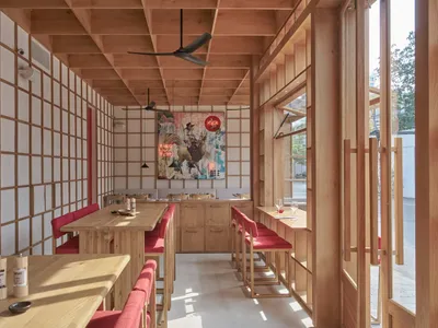 A modern restaurant interior featuring wooden furniture, a colorful mural, and red seating.