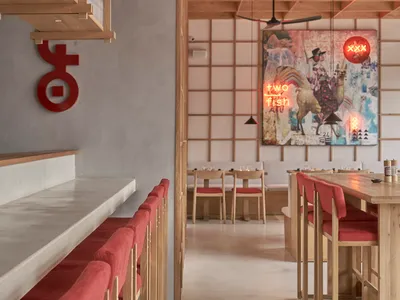 Modern restaurant interior featuring wooden tables, red cushioned seating, and a mural with two fish.