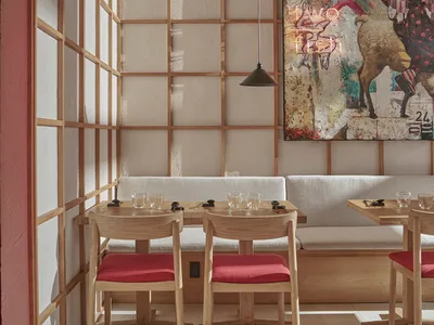 Modern restaurant interior with wooden tables and red cushions, featuring a colorful artwork on the wall.