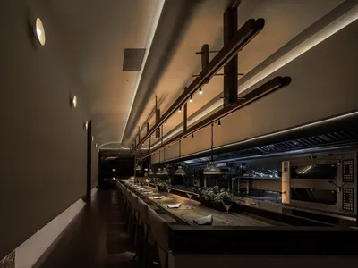 Long, open industrial restaurant bar with wood stools and hanging lights.