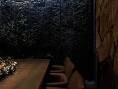 Industrial style restaurant interior with black stone walls, wooden table, and leather chairs.
