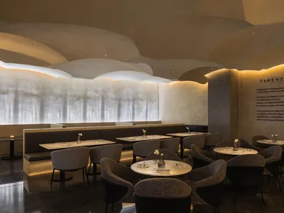 A modern restaurant interior with a concrete ceiling featuring circular shapes and warm, dim lighting.