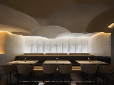 A modern restaurant interior with concrete walls, lit by warm, ambient lighting.