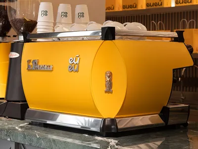 A bright yellow espresso machine sitting on a green marble counter.