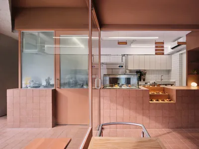 Contemporary cafe interior featuring a terracotta-tile half-wall with a display case showcasing pastries and a white-concrete