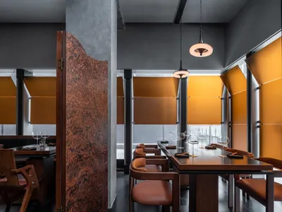 A modern restaurant interior with brown leather chairs, wooden tables, and metal pendant lights.