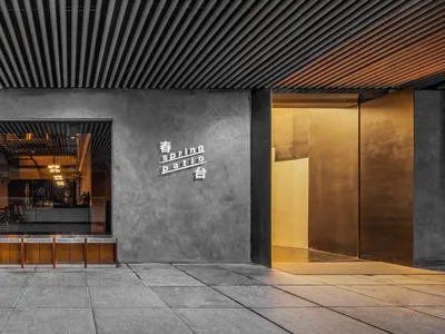 Modern minimalist restaurant entrance with concrete walls, glass doors, and wooden seating.