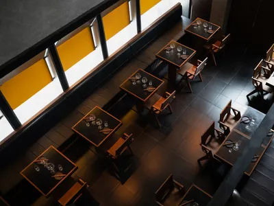 Modern restaurant interior with wooden flooring, square tables, and minimalist design.