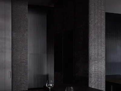 A sleek, minimalist restaurant bar with black concrete walls and counter, accompanied by elegant seating arrangements and emp