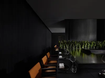A modern restaurant interior with dark black walls and floors, featuring green plants and minimalist design.
