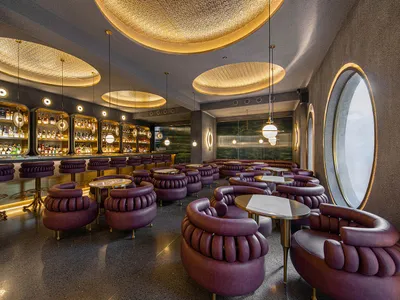 A modern industrial-style hospitality bar with purple leather furniture and circular light fixtures.