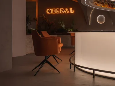 A modern restaurant bar with concrete, glass, and wood finishes, featuring a circular lighting fixture and a neon sign.