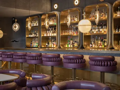 A sleek, modern restaurant bar featuring contemporary metal, leather, and glass elements.
