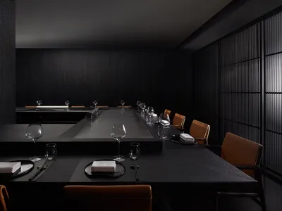 A modern restaurant interior featuring a sleek black stone dining area with minimalist decor and elegant table settings.