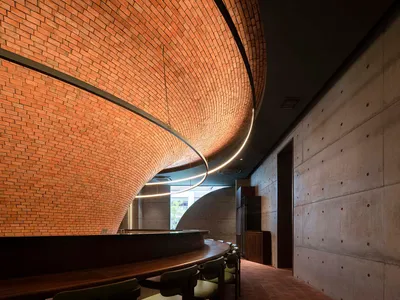 A modern, industrial-style restaurant interior featuring exposed brick walls and concrete elements, with a curved, brick-line