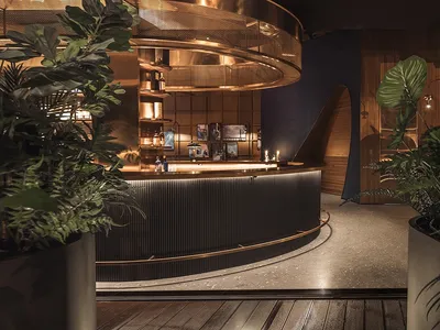 A modern bar interior with metal counter, wooden accents, potted plants, and warm lighting