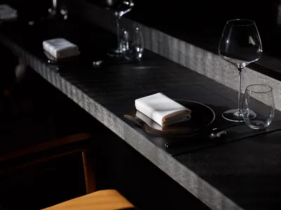 A modern restaurant counter with a concrete finish, featuring a minimalist design with black elements and sleek glassware.