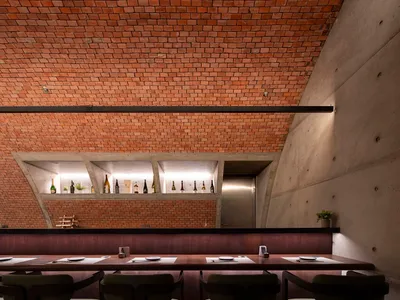 Industrial style restaurant interior with exposed brick ceiling, concrete walls, and a polished wooden table with place setti