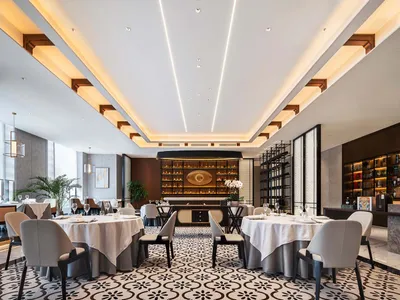 A modern restaurant interior with marble patterned floor, white tablecloths, and gray chairs.