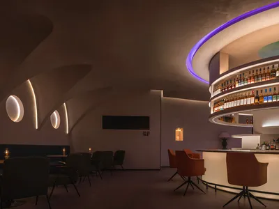 A modern industrial restaurant bar with concrete walls and ceiling, featuring a curved bar area with illuminated shelves and