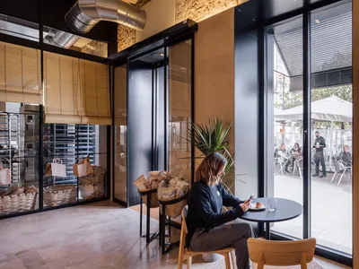 A person sitting at a small table in an industrial restaurant with metal pipes and glass walls.