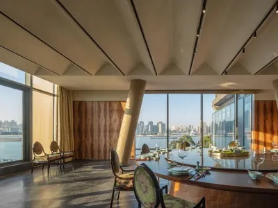 A stylish restaurant interior featuring metallic columns, a large glass window overlooking a cityscape, and a dining table se