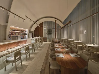Modern restaurant interior with wooden tables, glass walls, and fabric seating.