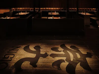 A modern, industrial-style restaurant interior with wooden flooring and booths.